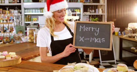 Portrait of smiling Caucasian waitress showing chalkboard with merry x-mas sign in cafe