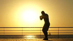 Silhouette of an athletic african american young man boxer standing and doing boxing training on pier