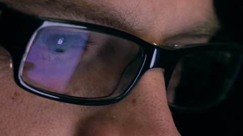 Eyes of serious young man in black rim glasses using his tablet computer. Screen reflecting in the glass. 4K close up shot
