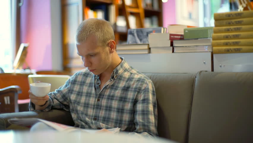 Student reading journal in the library and drinking coffee
