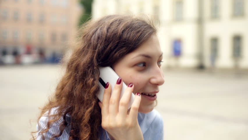 Girl chatting on cellphone and laughing at something on the square
