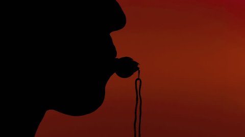 Silhouette shot of a woman blowing into a whistle. Red background.
