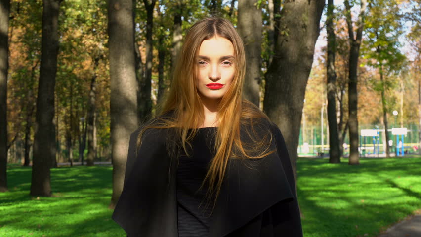 adorable young girl with red lips puts on stylish hat with a wide brim outdoors in the park