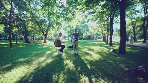 Music band. Duet. Ensemble. Singer and performer. Song's author. Singer and musician. Two men play a guitar outdoors in summer park. One of the musicians singing into the microphone. Two guitars.