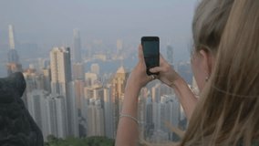 Making photos of city skyline. Travel in Hong Kong. Teenage girl making self portrait right before the sunset at the Victoria Peak.  