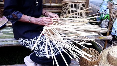 Elderly female hands manually weaving bamboo basket. 