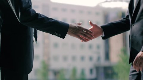 Two business men shake hands against business center background