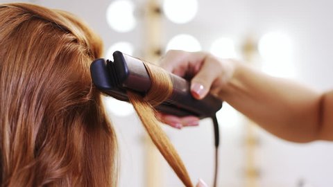 Hairdresser curling hair to foxy girl in beauty salon Close up Slow motion