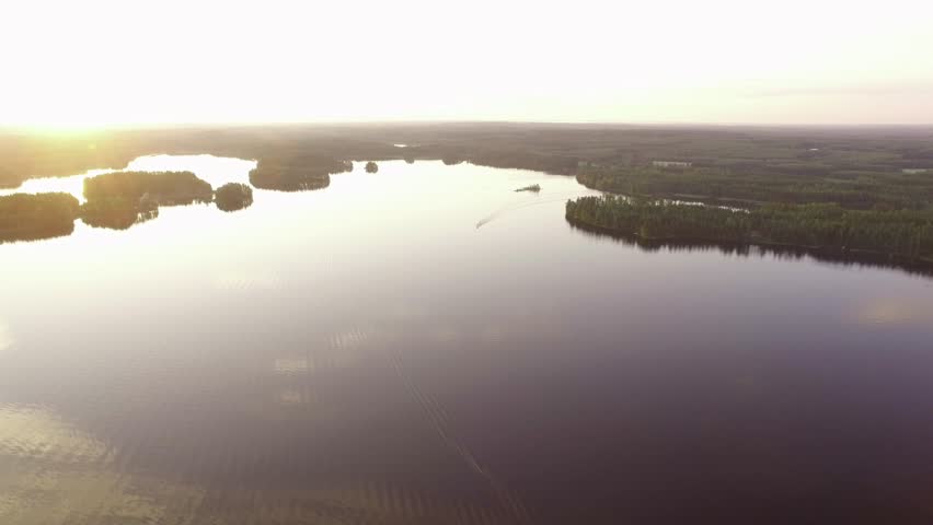 Aerial midsummer evening overfly shot of a motorboat driving in beautiful lake landscape at Puruvesi, Finland, leaving a trail on the calm water surface.