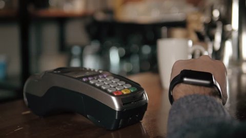 Customer paying with NFC technology by smart watch contactless on terminal in modern cafe