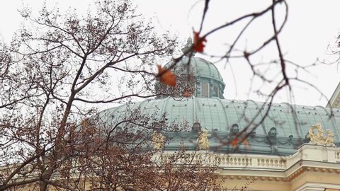 ODESSA, UKRAINE - FEBRUARY 10, 2016: Odessa Opera and Ballet Theater on cloudy sky background. Winter trees with orange leaves and acorns close up, domed theater roof with balustrade sculptures afar.