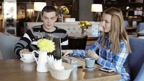 Boy and girl in the cafe at the table. People use laptop and smartphones, talk, smiling, laugh and drink coffee.