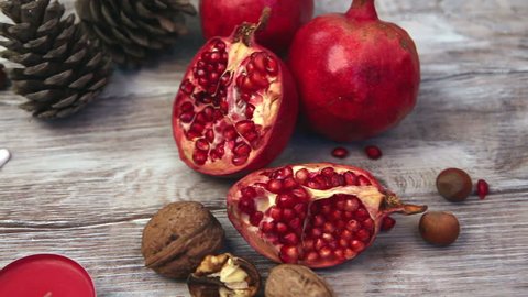 Female hand places Christmas gift box on wooden rustic background with fresh pomegranates and nuts