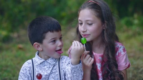 Beautiful little children eat lollipop candy in the garden.