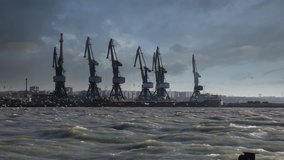 Video shot of cargo cranes with dramatic sky and storm wind in the sea port 
