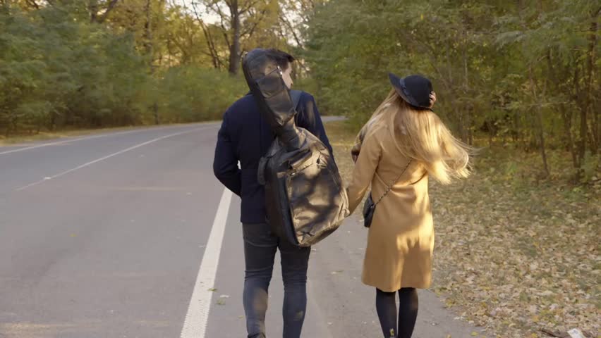 Boy with guitar and blonde girl walk along the road