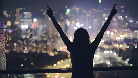 Young beautiful woman dancing on terrace during night. Young excited woman dancing on the rooftop, enjoying breathtaking view over the city at night. City lights, Party time.  