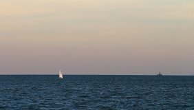 White sailboat in the distance sailing to Venice on blue waves in the Adriatic sea at sunset