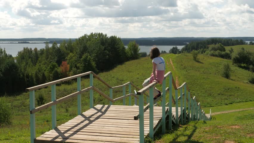 Child sitting on railing looks afar, runs down away to the road.