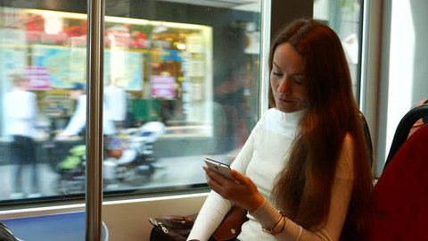 Thoughtful woman stare to phone, travel in tram at shopping street. Typical passenger bend head over mobile device, city life flash outside. Helsinki tourist use cheap public transport for short trips