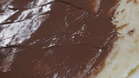 Knife spreads chocolate topping on sweet surface 4K 2160p 30fps UltraHD tilting footage - Spreading hazelnut creme over pancake texture close-up 3840X2160 UHD video