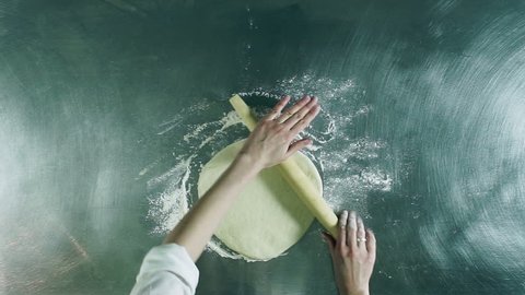 Cooking a pizza. Pretty young woman rolling out a dough with a rolling pin. Top view. HD