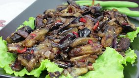 Baked eggplant with onions, garlic, red hot chili pepper and walnuts on the black plate, close up. Rotates plate with eggplant, onions, garlic and red hot chili pepper