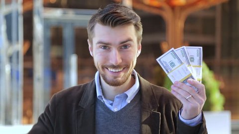 Happy man holding in his hand bundles of money cash dollars and showing thumbs up
