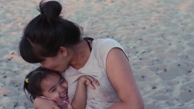 Young mother and baby daughter hugging on the beach.