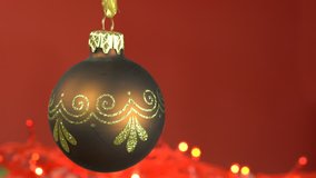 Single dark golden bauble on dark red background, simple Christmas background video with room for text on right side, subtle lights flickering in lower third, video for seamless looping.