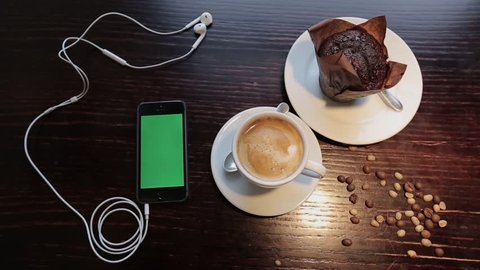 Cup of coffe with marshmellou, muffin and cellphone with green in cafe
