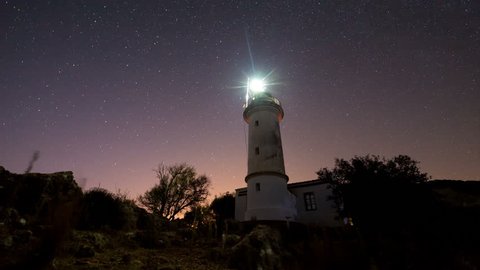 4K. Timelapse of beautiful night landscape with lighthouse with rotating starry sky on a background