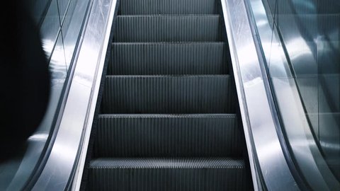 Close-up shot of young man with bag moving on escalator,  traveling on train. Rush hour, subway underground station. Modern escalator stairs moving up.