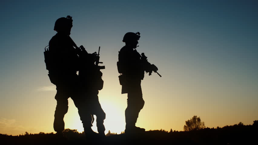 Squad of Three Fully Equipped and Armed Soldiers Standing in Desert Environment in Sunset Light. Slow Motion. Shot on RED EPIC Cinema Camera in 4K (UHD).