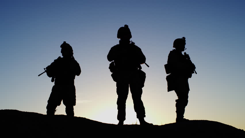 Squad of Three Fully Equipped and Armed Soldiers Standing in Desert Environment in Sunset Light. Slow Motion. Shot on RED EPIC Cinema Camera in 4K (UHD).