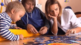 Happy caucasian family assembling puzzle together. Parents and their little boy having free time at home. 4K video