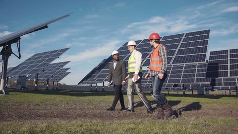 Technician walks with workman and investor through field of solar panels