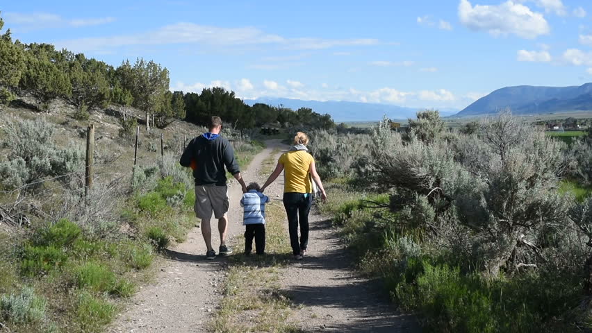 SANPETE COUNTY, UTAH - MAY 2015: Young family and dog walk away holding hands down sagebrush-lined country lane on sunny afternoon with sun getting low in the sky. | Shutterstock HD Video #20864602
