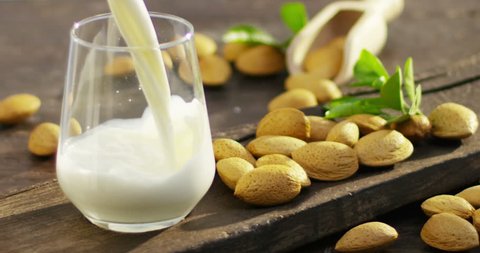 The almond milk is poured into a glass in slow motion, the background in woods there are almonds, perfect for a diet for a healthy diet and can be used as medicine. concept: diet, fitness, medicine.