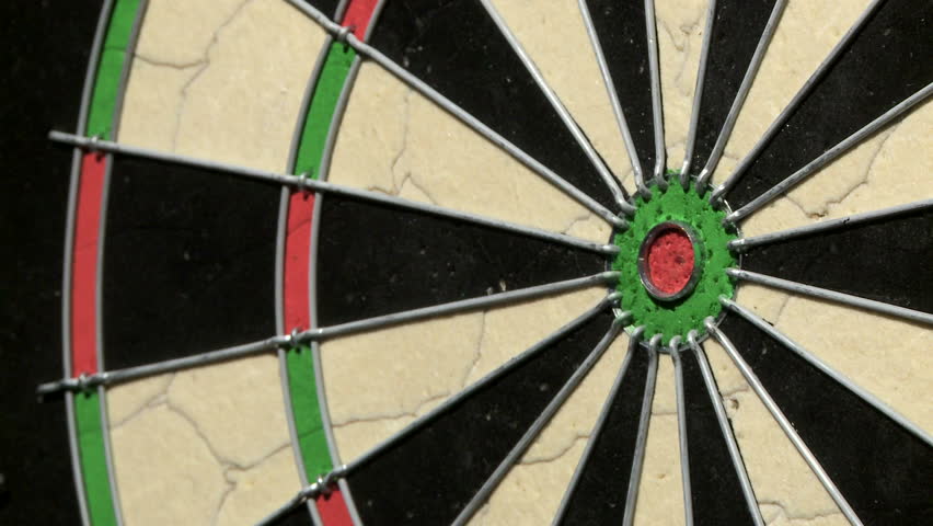 Medium shot of a single dart hitting a bull's eye on a dart board