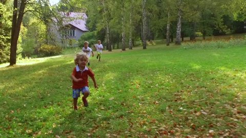 Three active boys running outdoors near the house in autumn. Slow motion.