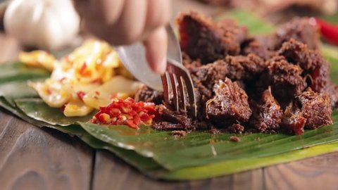 Woman eating rendang jerky beef stew with mustard leave and sambal