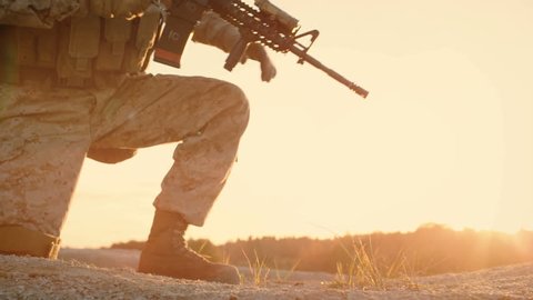 Side view Soldiers Lie Down on the Hill, Aim through the Assault Rifle Scope in Desert Environment in Sunset Light. Slow Motion. Shot on RED EPIC Cinema Camera in 4K (UHD).