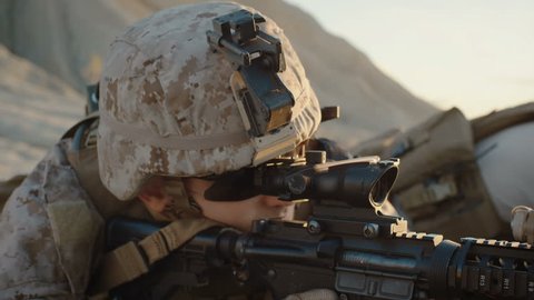 Close-up of Soldier Lies Down on the Hill, Aims through the Assault Rifle Scope in Desert Environment. Slow Motion. Shot on RED EPIC Cinema Camera in 4K (UHD).