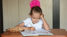 Seven-year girl schoolgirl doing homework distracted and looked into the frame