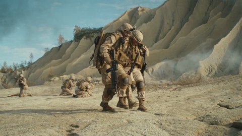 Soldiers Carrying Injured One While other Members of Squad Covering Them During Military Operation in the Desert. Slow Motion. Shot on RED EPIC Cinema Camera in 4K (UHD).