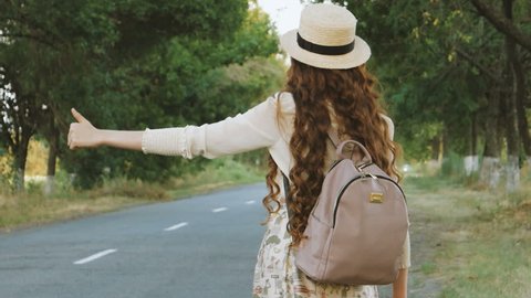 Hitchhiking tourism concept. Portrait of travel hitchhiker woman with hat and backpack walking on road during holiday travel