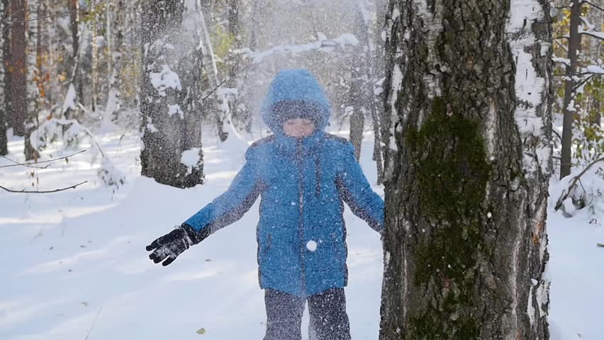 kid playing throwing snowballs from behind tree in winter Park