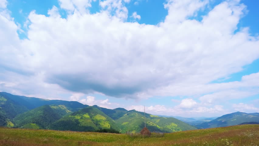 Timelapse of Clouds Passing by Summer Landscape with Haystack on a Foreground and Mountains on the Background. 4K. 
