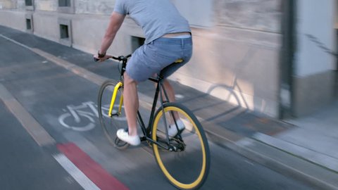 Young hipster man in casual summer cloths riding his fixed gear bike along the bike lane on city street ஸ்டாக் வீடியோ